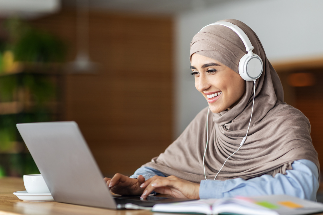 Cheerful muslim woman studying online, cafe interior